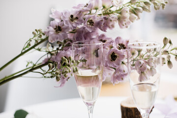 Two glasses of white wine, wine bottle, with delphinium flowers on the white table on the background