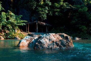 Beautiful shot of a tropical bamboo house at the beach with a huge rock in a water