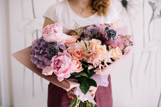 Very nice young woman holding big and beautiful bouquet of fresh roses, carnations, peony, matthiola in tender pink and purple colors, cropped photo, bouquet close up