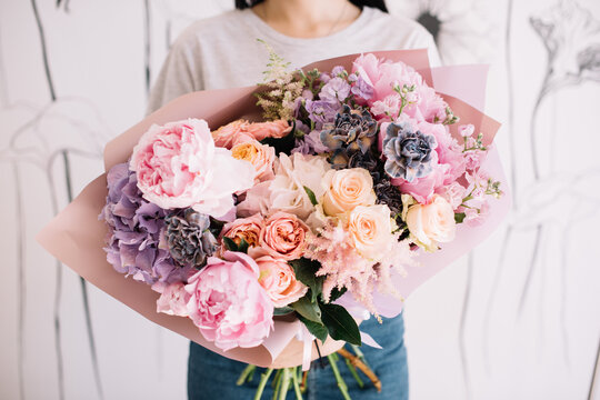 Very nice young woman holding big and beautiful bouquet of fresh roses, carnations, peony, matthiola in tender pink and purple colors, cropped photo, bouquet close up
