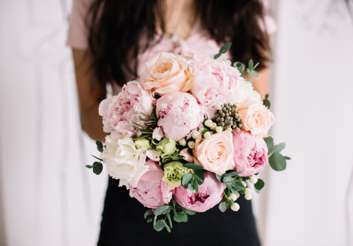 Very nice young woman holding big and beautiful wedding bouquet of fresh peony, roses, eustoma, brunia, eucalyptus in pastel cream and pink colors, cropped photo, bouquet close up