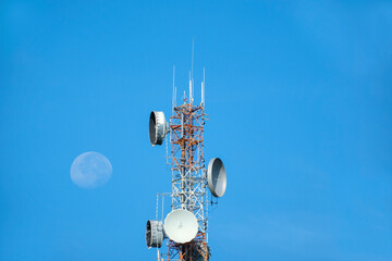 Radio transmission towers. On the background the moon was indistinct from the brightness and the blue sky.
