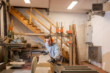 Fototapeta premium Young carpenter boy, concentrated on his job while cutting a long plank of wood with a circular saw.