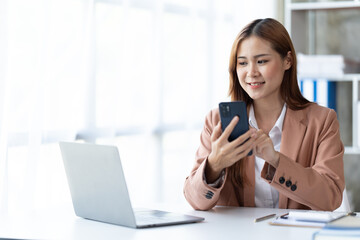 Fototapeta na wymiar Asian businesswoman in formal suit in office happy and cheerful during using smartphone and working.
