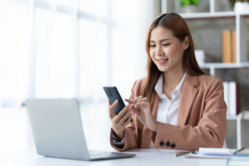 Asian businesswoman in formal suit in office happy and cheerful during using smartphone and working.