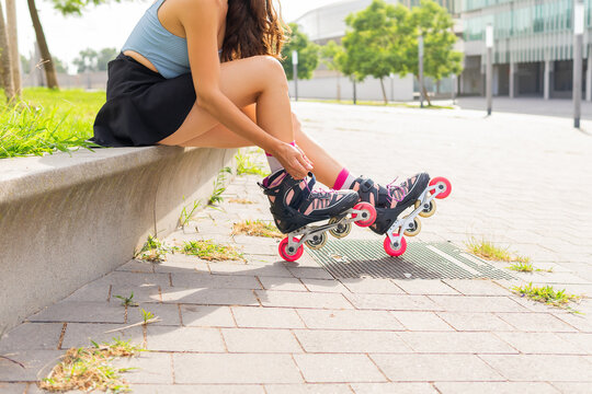 Anonymous active young woman wearing roller blades sitting on bench in city