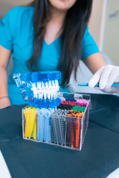 Crop female dentist choosing plastic bands for braces in dental clinic