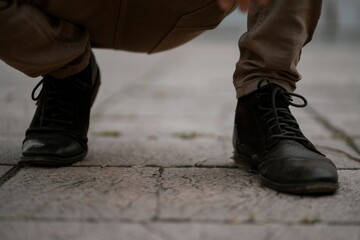 Partial view of a man in the squat position wearing black shoes and a navy green jeans