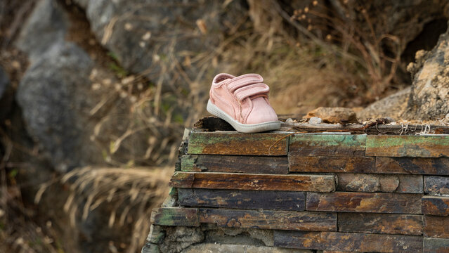 Pink Lost Baby Boot Lost During Escape, Lost On The Street Children's Shoes. A Woman's Hand Takes A Small Sneaker In Her Hand.