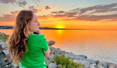 a teenage girl in a Green T-shirt stands with her back to the camera and shoots a beautiful sunset...
