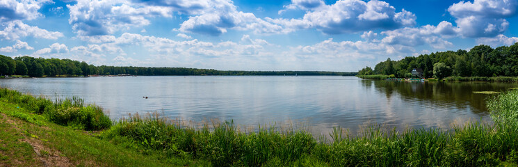 Panoramic view of the lake on a sunny day. Floating sailboats and a forest in the background. Paprocany Lake, Tychy, Poland.