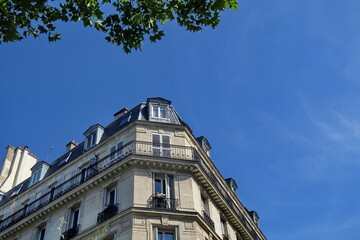 Fototapeta na wymiar Immeuble ancien en coin de rue. Façade blanche, ciel bleu et feuillage vert.