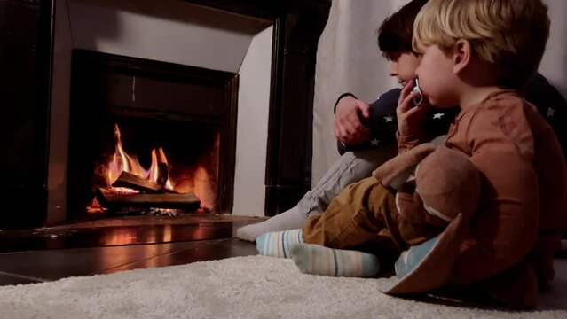 Two boys getting warm sit in front of fireplace