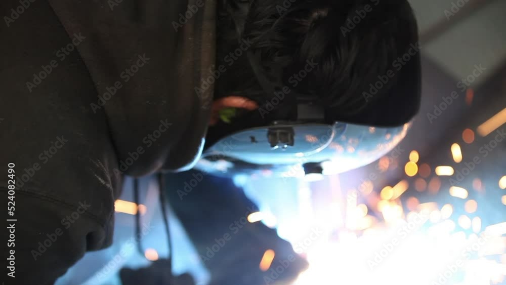 Poster welder working hard on metal fabrication and removing face field to check the work as he progresses.