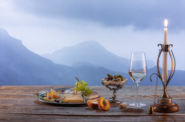 Fototapeta premium Vintage image of wine bottle, glass filled with delicious white wine isolated over beautiful nature landscape of mountains. Winemaking on countryside