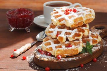 Waffles with berries sprinkled with powder. With jam and a cup of tea on a wooden background