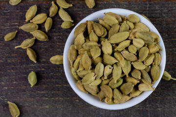 Green Cardamom on white bowl on rustic wooden table, top view. Cardamom is a fragrant herb used as an ingredient for cooking. 