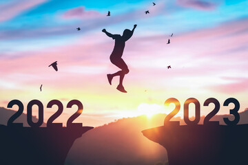 Silhouette man jumping between cliff with number 2022 to 2023 and birds flying at top of mountain. Freedom challenge and travel adventure holiday concept.
