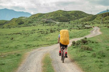Fototapeta premium rear view of a hiker cyclist who rides along a dirt rocky road to the top of a hill along a high-altitude route