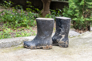 A pair of dirty black rubber boots is on a path in the garden after using