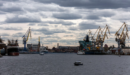 Fototapeta premium Water landscape in the lower reaches of the Neva River with cranes and ships at the mooring wall.