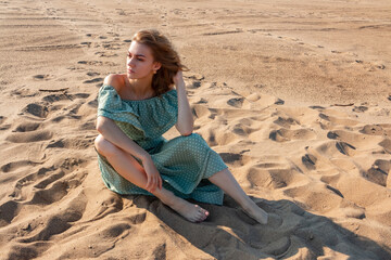 The girl is sitting on the sandy beach.