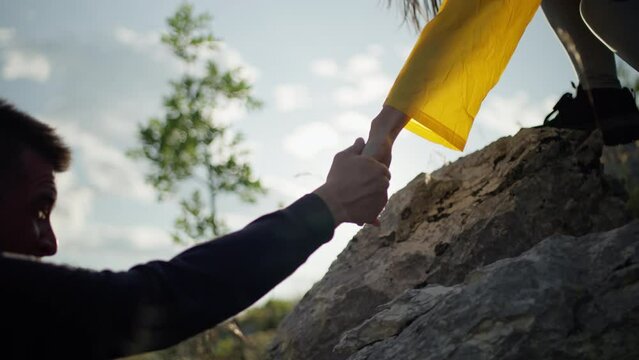 Close-up of a girl helping a boy climb a rock. Mutual aid during a hike in the mountains, a support woman gives a hand to a man during climbing. High quality 4k footage