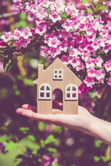 The girl holds in her hand the symbol of the house against the background of blooming weigela
