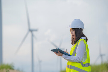 women engineer working and holding the report at wind turbine farm Power Generator Station on mountain,Thailand people