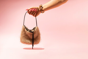 Female hand with golden bracelet holding little bag isolated on pink background