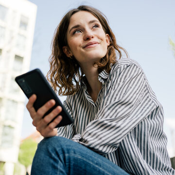 Young woman smiling looking to the side with cell phone in hand