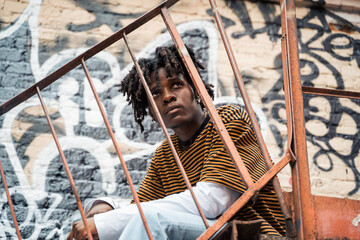 Young handsome stylish black man with natural hair dreadlocks. Afroamerican guy.Stairs,wall painted with graffiti in poor quarter of street art culture city district.African american skateboarder man