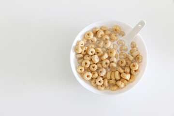 Top view of cheerios in bowl of milk with spook on right side of white table background, a healthy morning oat cereal with low sugar and high fibre for breakfast, copy space on left