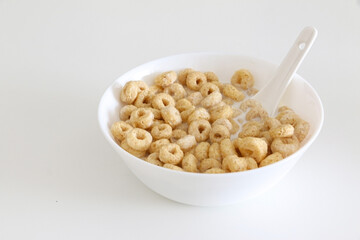 Close up of cheerios in a bowl of milk with spoon on right of white table background, healthy...