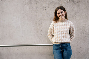 Young woman leaning against concrete wall and looking at camera