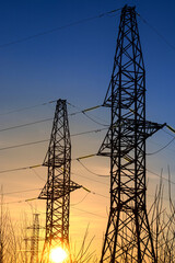 Electricity poles and electric power transmission lines against at sunset on a winter day with flickering air. High Voltage towers provide power supply over a long distance.