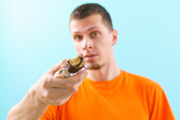 Man proposing to eat a milk chocolate bar is packaged in the plastic paper on blue background. Nougat. Cinnamon. Cream. Caramel. Creamy. Walnut. Fresh. Eats. Foodstuff. Nutriment. Nourishment