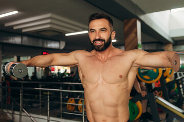 Fototapeta na wymiar athletic man doing exercises with dumbbells with a bare torso in the gym