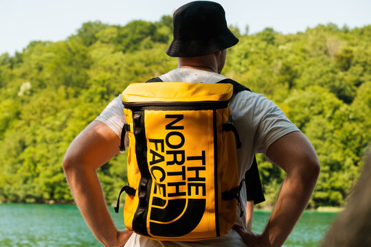 Tourist with yellow The North Face backpack standing near the lake, July 2022, Rijeka, Croatia.