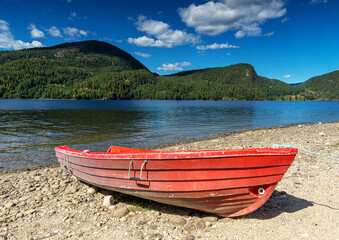 Fototapeta na wymiar red boat on the pebble beach at the lake in Norway