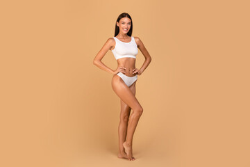 Young slender caucasian lady posing in white underwear over beige studio background, full length...