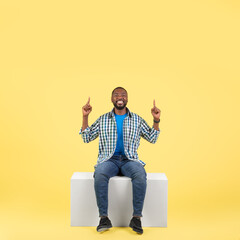 Black Guy Pointing Fingers Up Sitting Over Yellow Background, Square