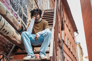 Young handsome stylish black man with natural hair dreadlocks. Afroamerican guy.Stairs,wall painted with graffiti in poor quarter of street art culture city district.African american skateboarder man