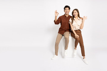 Young Asian businessman and businesswoman smiling and showing OK sign and sitting on white box isolated on white background