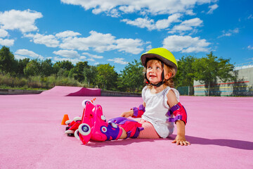 Little girl learn to skate rollers, sit smiling on the floor