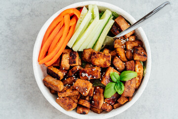 Top view bowl with roasted tempeh made of fermented soy beans, fresh vegetable sticks with sauce and sesame seeds. Plant based protein. Healthy cooking and eating. Go vegan. Flat Lay, selective focus.
