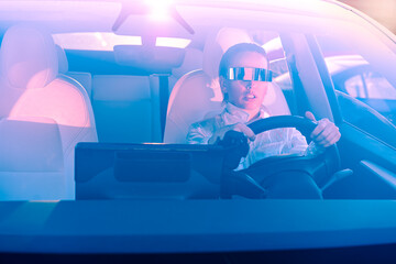 Fashion cyberpunk girl driving a supercar. Woman with futuristic eyeglasses sits by the car steering wheel. Future technology concept. Pink and blue toning. Selective focus, copy space.