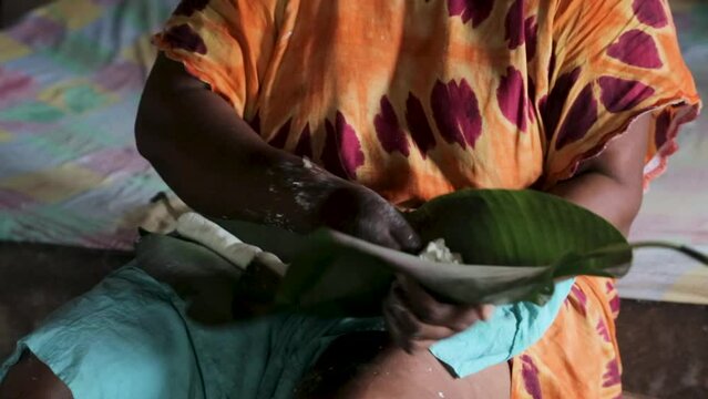 African woman wrapping crushed cassava tubers in banana leaves. African traditional cuisine.  Africa. Equatorial Guinea. Inside an African house.