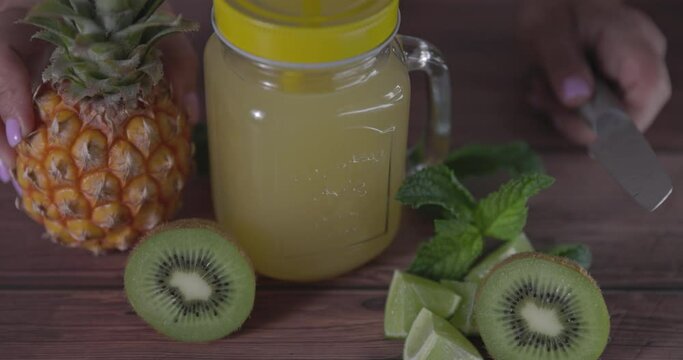 Natural juice mug with pineapple, kiwi and lime. With blurred woman's body in background.