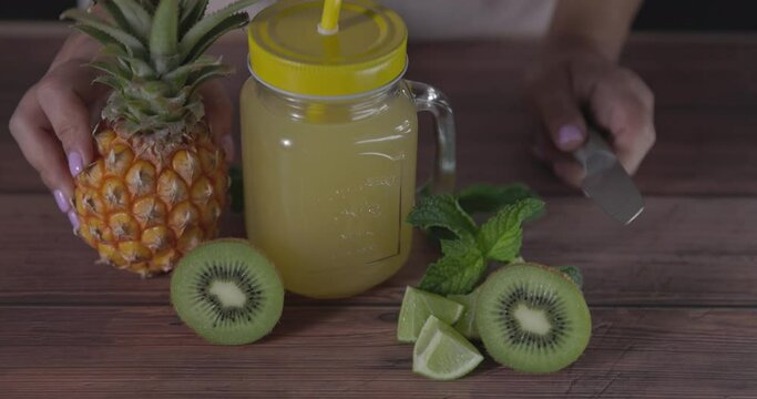 Natural juice mug with pineapple, kiwi and lime. With blurred woman's body in background.